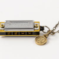 Sideways view of Genuine Hohner harmonica necklace with brass charm with text "Here for Now"