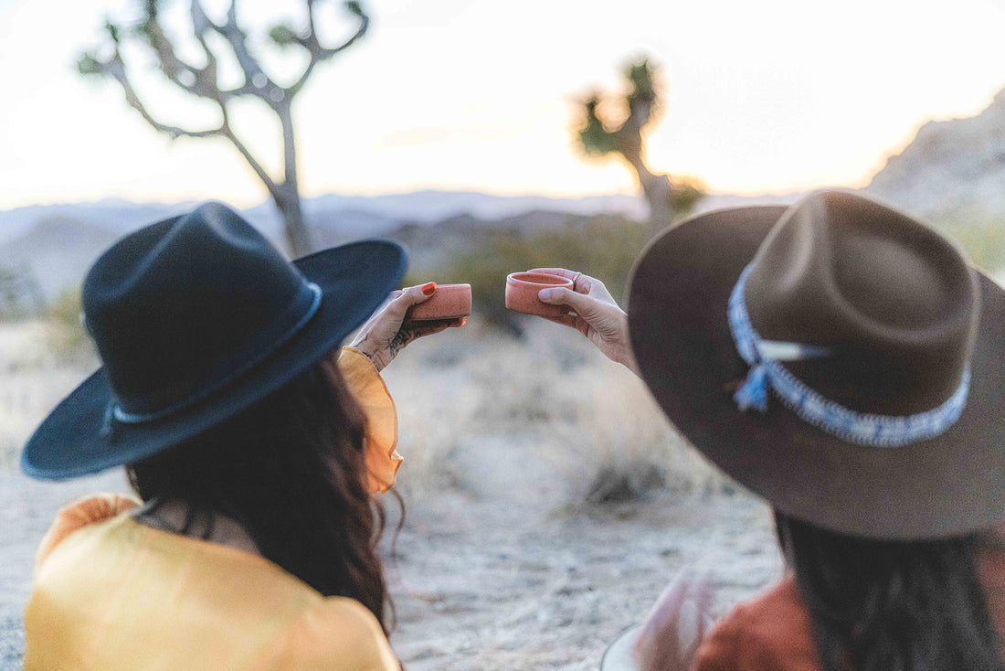 Two women toasting in the desert with the pink mezcal copitas
