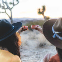 Two women toasting in the desert with the pink mezcal copitas