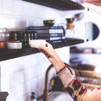 Woman in kitchen grabbing the white speckled clay mezcal copita from a shelf