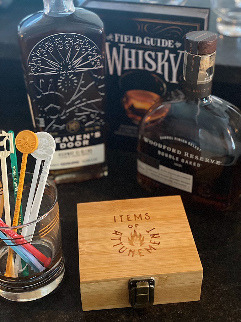 Whiskey stone set wooden box with brass clasp featuring text "Items of Attunement" and whiskey bottles in background
