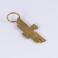 Brass keychain with thunderbird design that doubles as a bottle opener laid flat at a diagonal