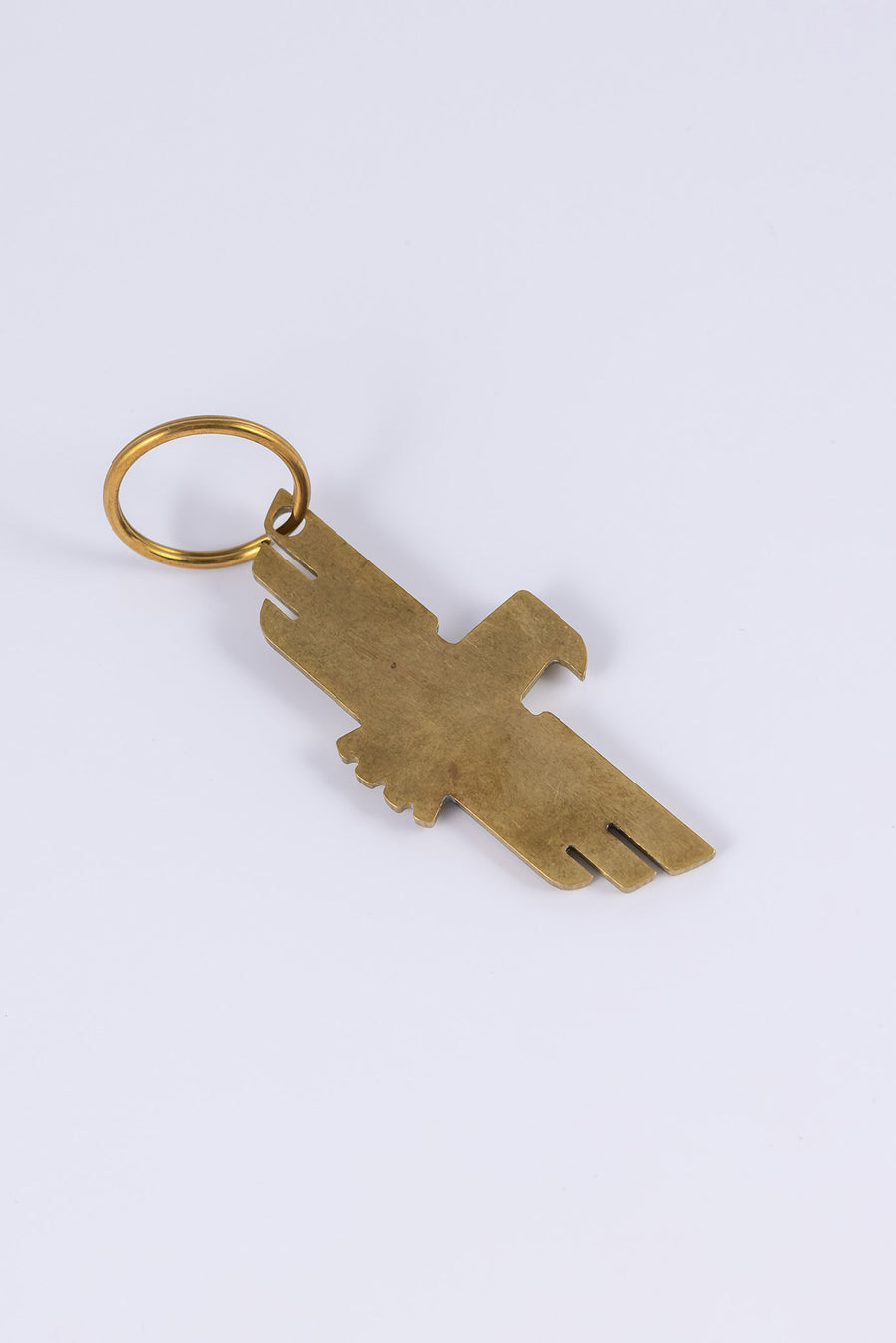 Brass keychain with thunderbird design that doubles as a bottle opener laid flat at a diagonal