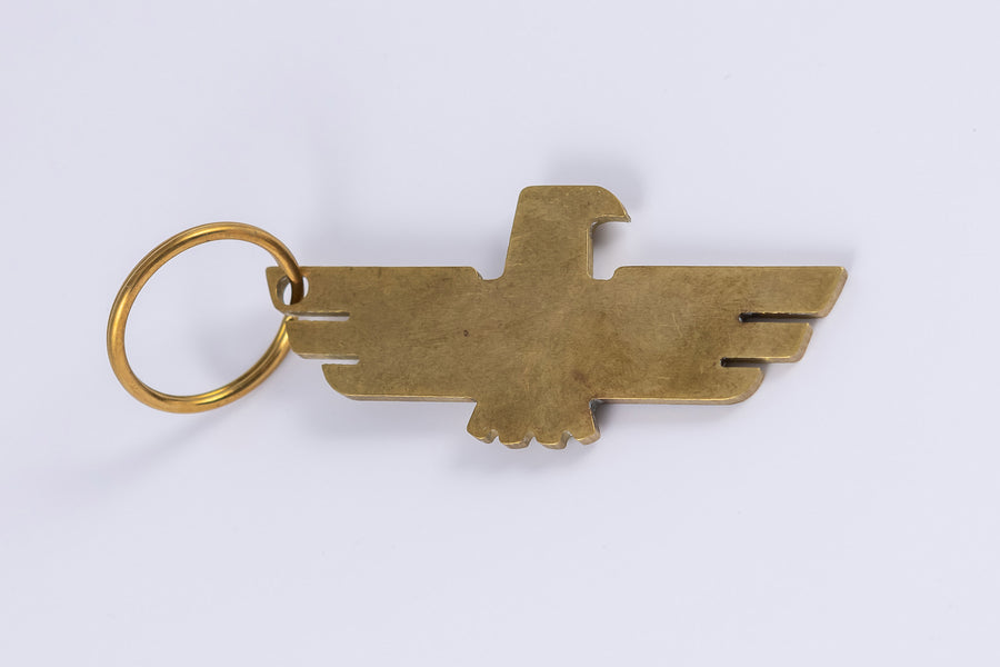 Brass keychain with minimalist thunderbird design that doubles as a bottle opener laid flat horizontally