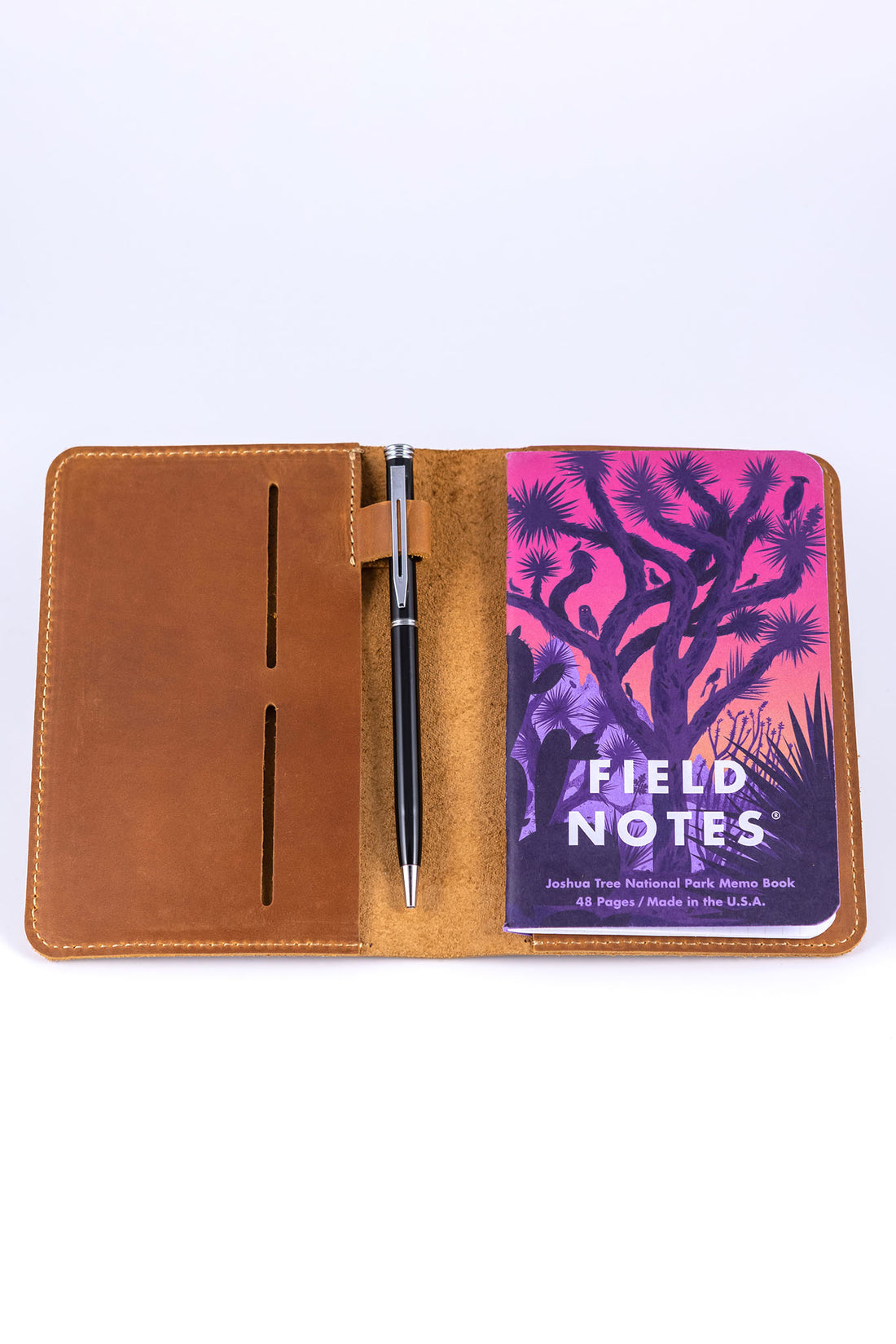 Leather field notes wallet and traveler's notebook cover open to reveal a strap with a pen attached and a field notes memo book tucked within the internal pocket