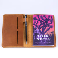 Leather field notes wallet and traveler's notebook cover open to reveal a strap with a pen attached and a field notes memo book tucked within the internal pocket