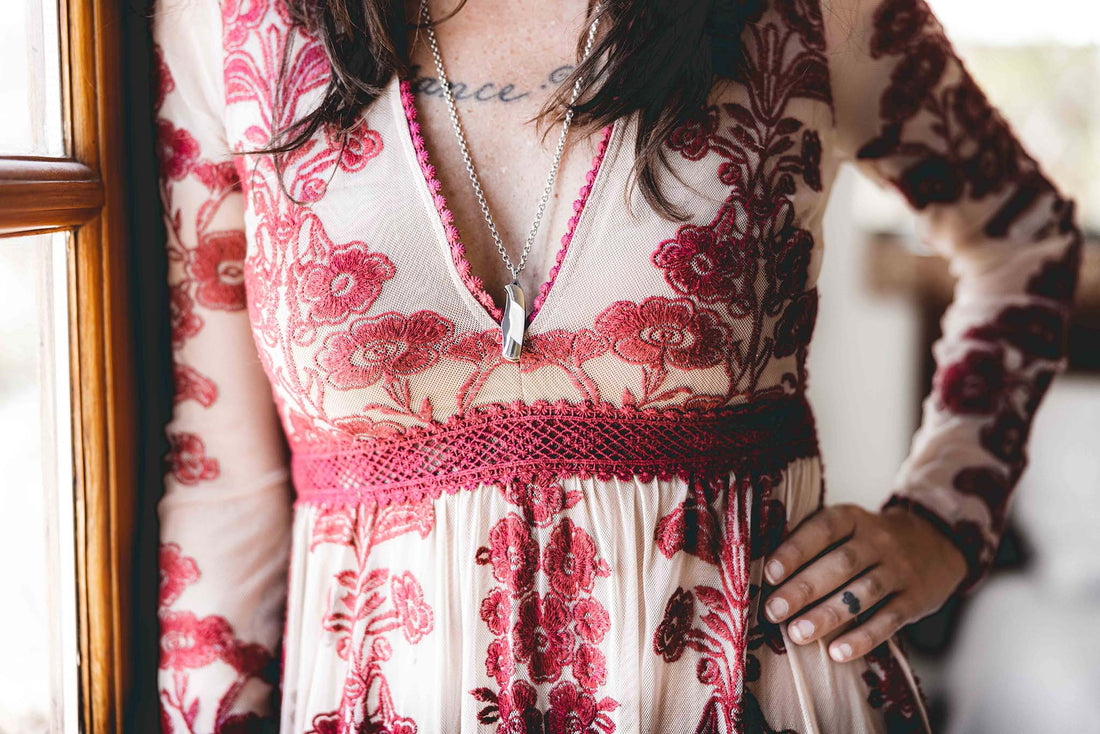 Woman wearing mini pocket knife necklace with mother of pearl over a tan and red embroidered dress