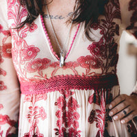 Woman wearing mini pocket knife necklace with mother of pearl over a tan and red embroidered dress