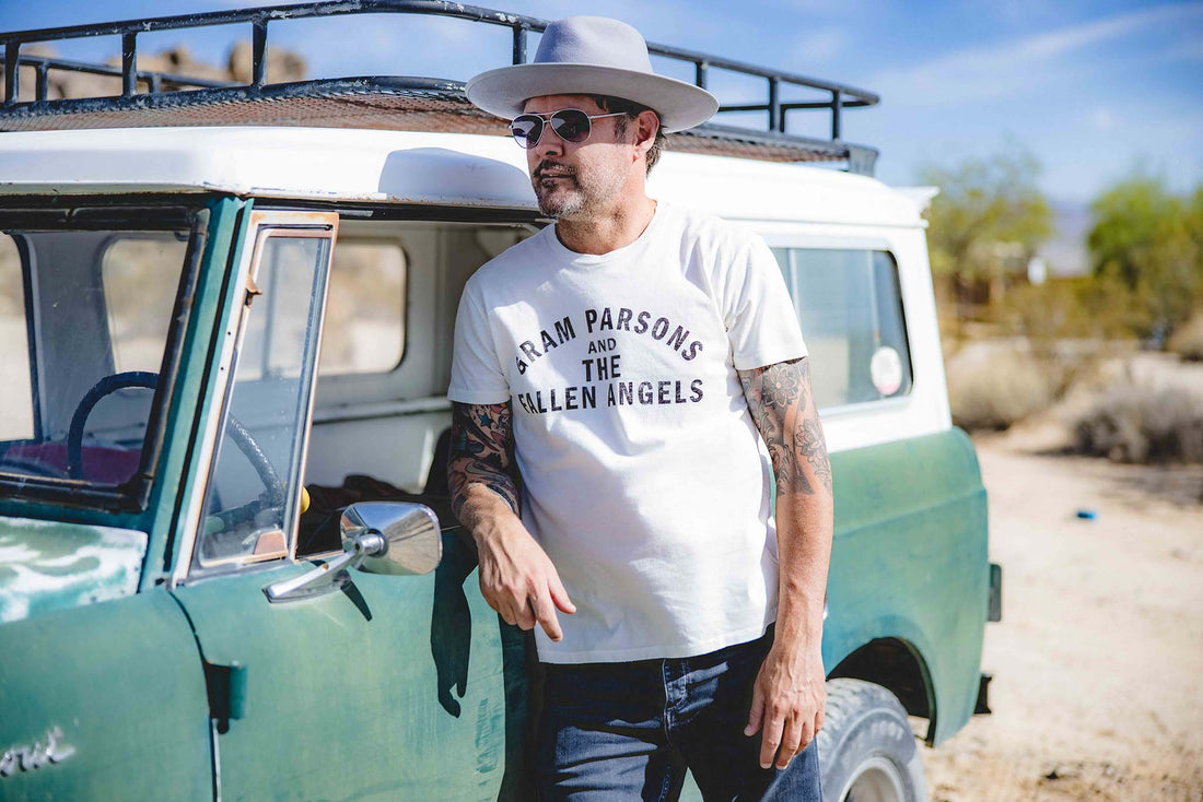 Man leaning on side of car wearing Gram Parsons Fallen Angels t-shirt and wool hat