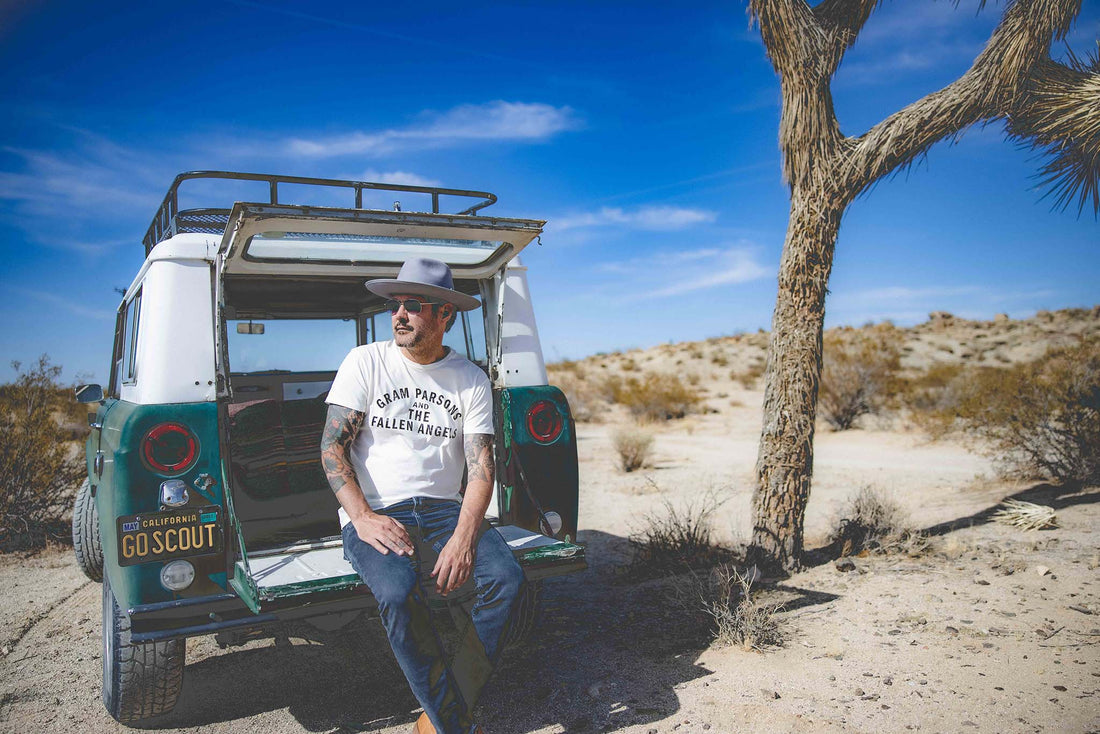 Man sitting at back of his car wearing Gram Parsons and the Fallen Angels tshirt in California desert