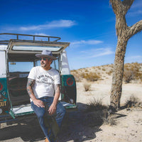 Man sitting at back of his car wearing Gram Parsons and the Fallen Angels tshirt in California desert