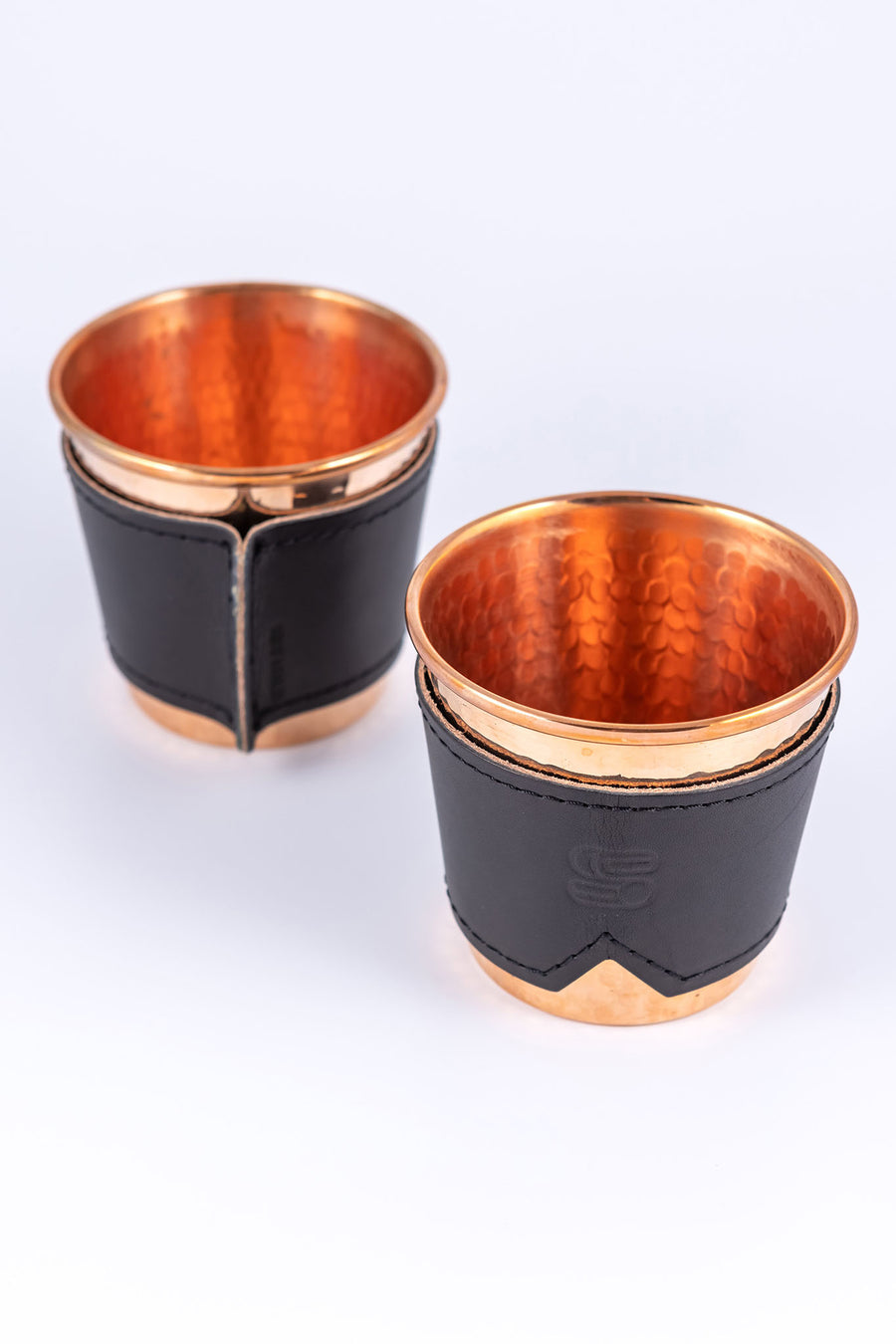 Two hammered copper cups with black leather sleeves stamped with Sound As Ever Logo on the front and the sewn seam in the back