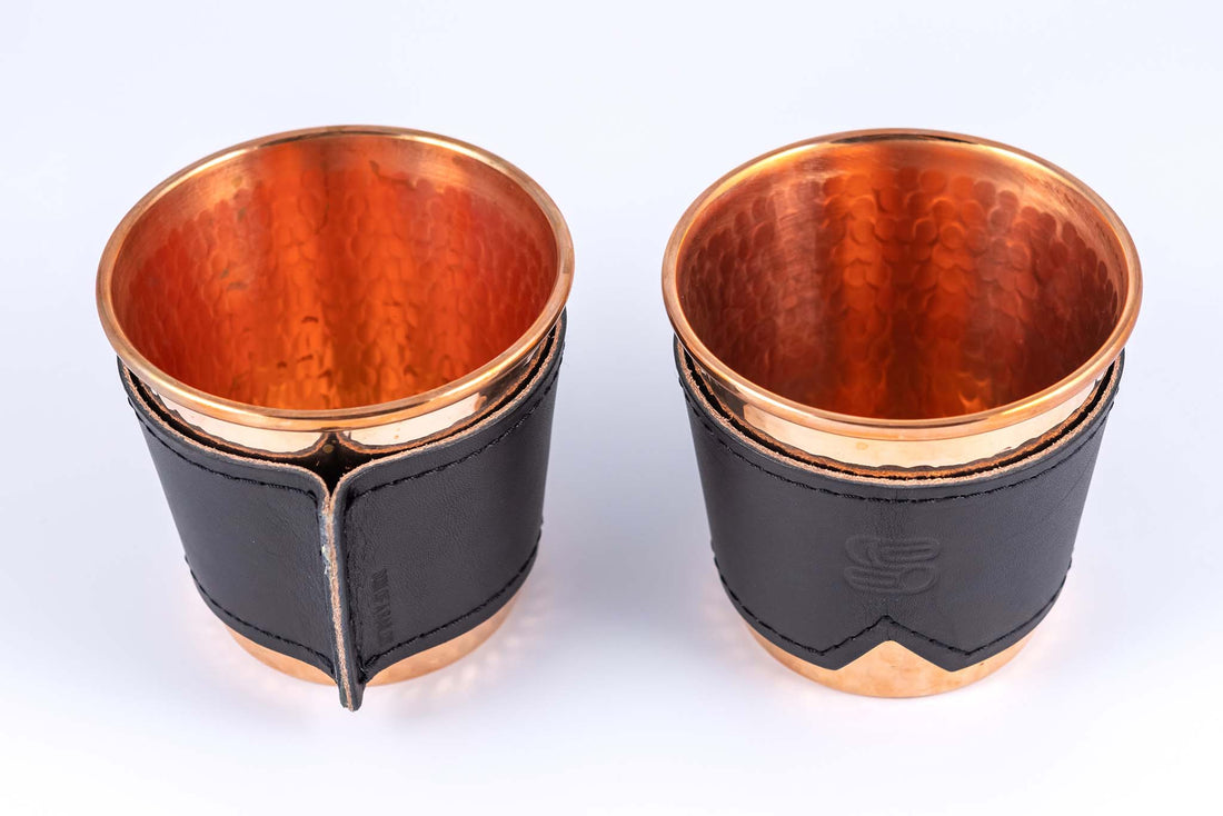 Two hammered copper cups with black leather sleeves stamped with Sound As Ever Logo on the front and the seam in the back with black stitching