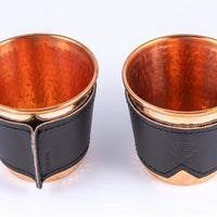 Two hammered copper cups with black leather sleeves stamped with Sound As Ever Logo on the front and the seam in the back with black stitching