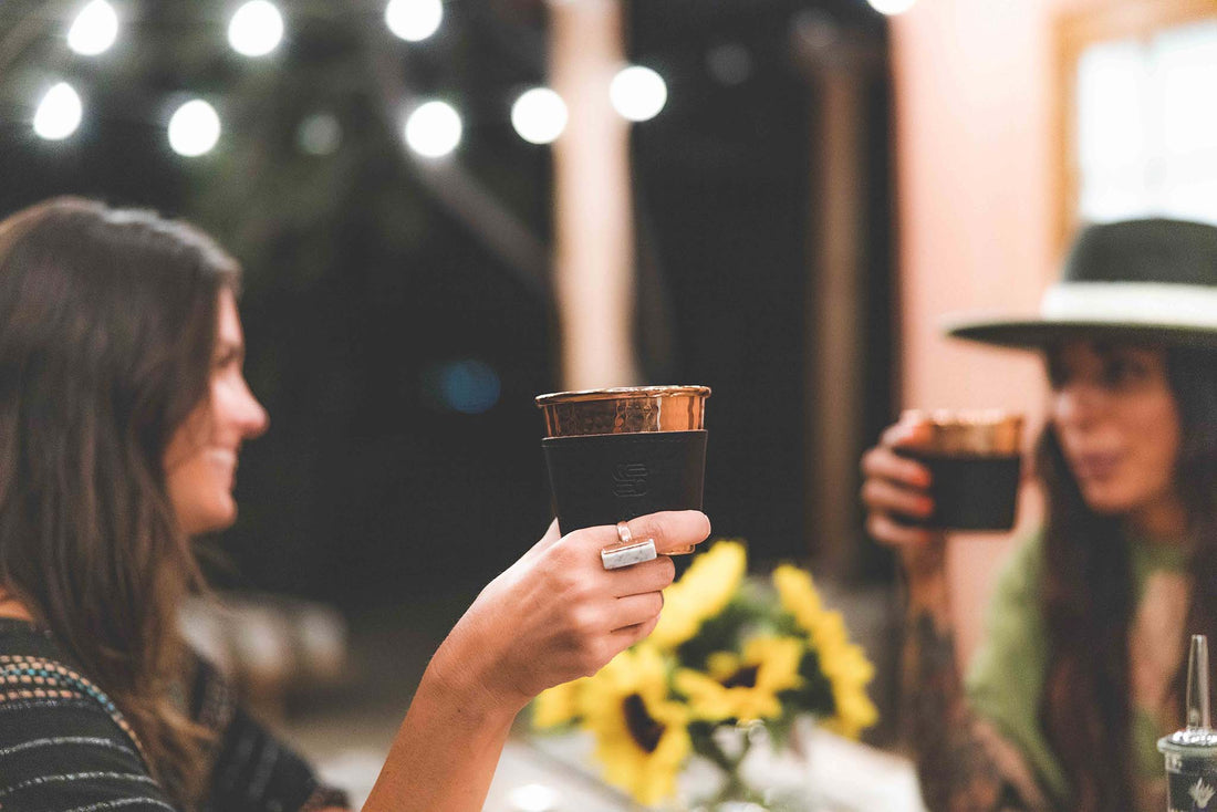 Two women having drinks at night drinking from the hammered copper cups with black leather sleeves