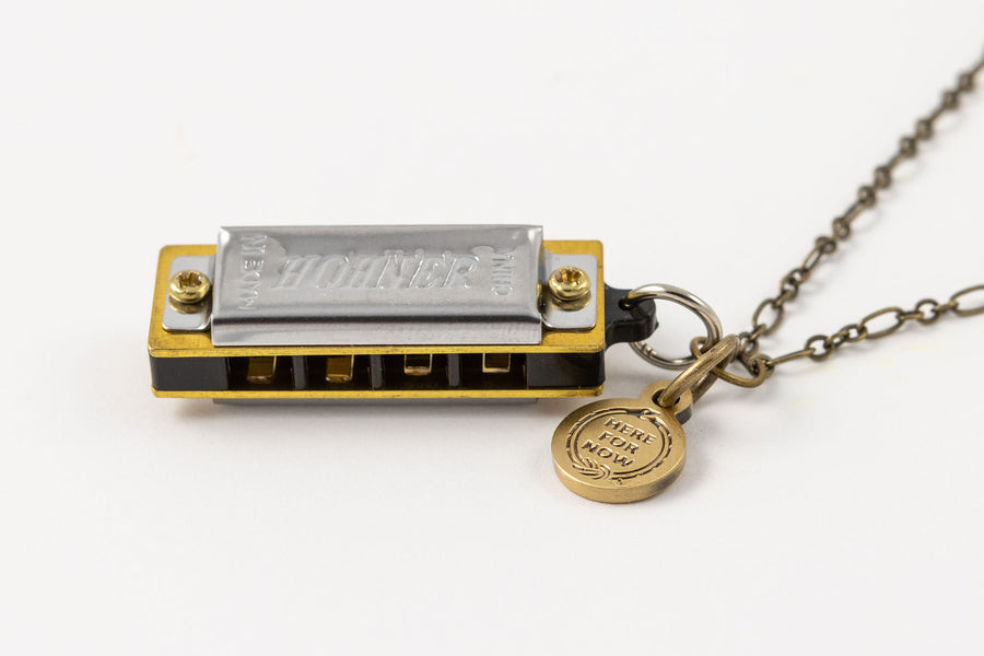 Sideways view of Genuine Hohner harmonica necklace with brass charm with text "Here for Now" 