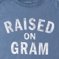 Close up view of blue graphic t-shirt for kids with white text "Raised on Gram"