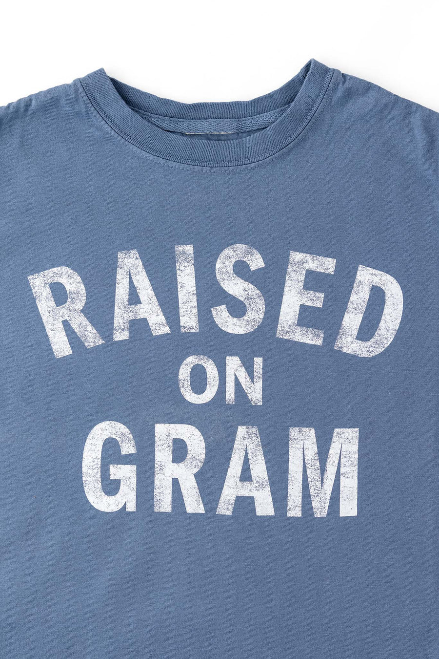 Close up view of blue graphic t-shirt for kids with white text "Raised on Gram"