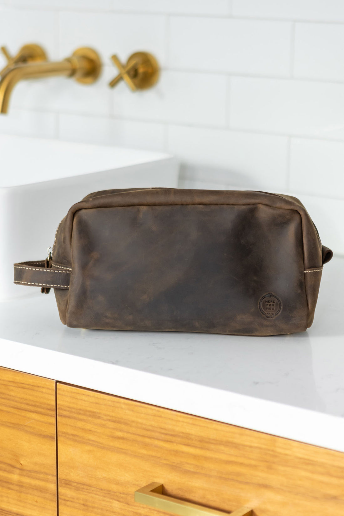 Leather dopp bag from Sound As Ever in dark brown umber color with the embossed "Here For Now" Ouroboros design and zip closure and off-white stitching