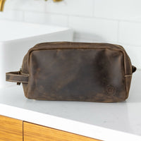 Leather dopp bag from Sound As Ever in dark brown umber color with the embossed "Here For Now" Ouroboros design and zip closure and off-white stitching