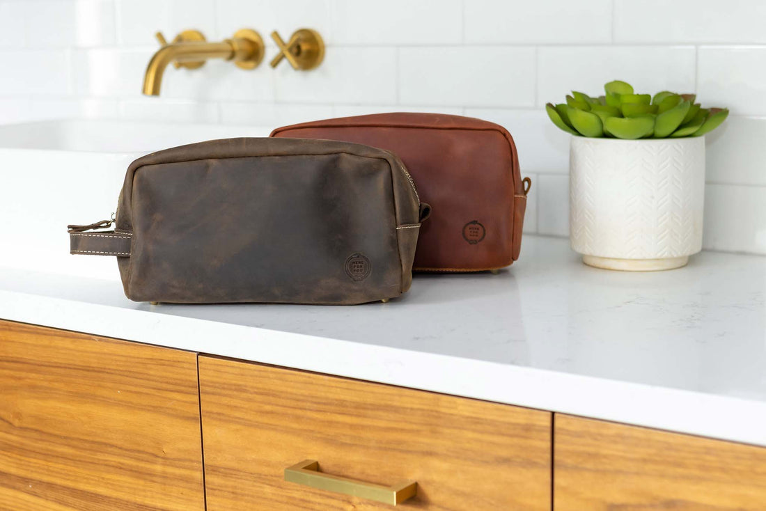 Close up of the leather dopp bags from Sound As Ever in two color variations- a dark chocolate brown and a rich reddish brown- with the embossed "Here For Now" Ouroboros design