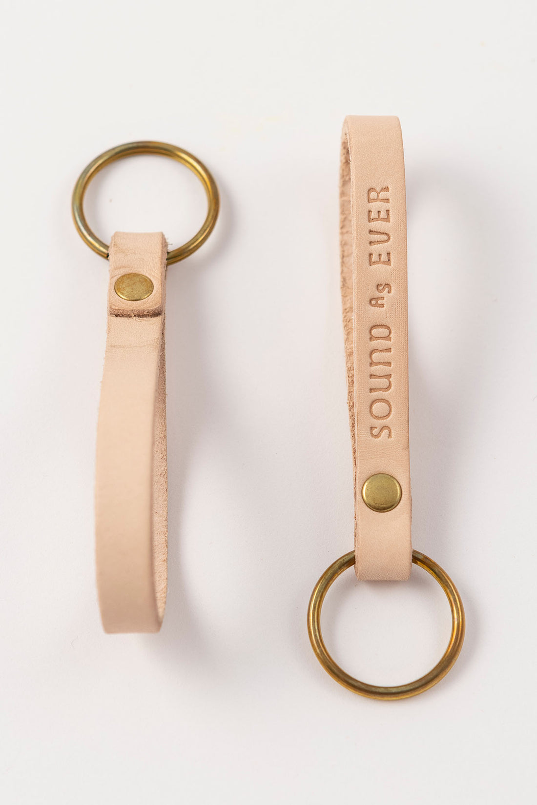 Tan color leather keychain with brass ring stamped with text "Sound as Ever"
