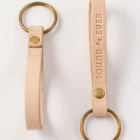 Tan color leather keychain with brass ring stamped with text "Sound as Ever"