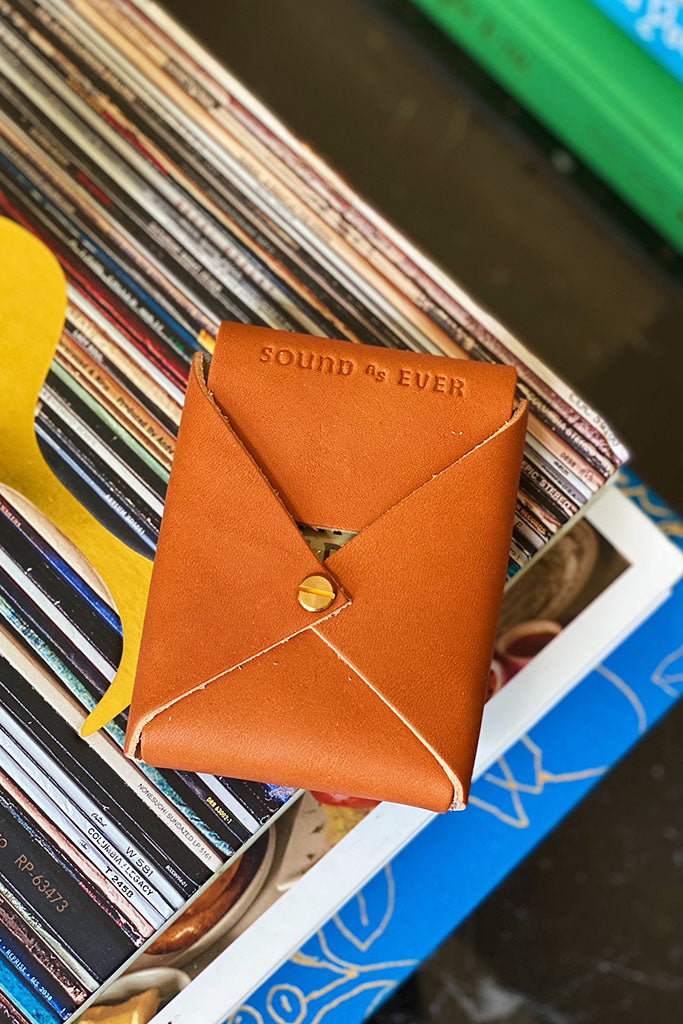 Leather playing card case on top of books clearly displaying stamped letters "Sound As Ever" on opening flap