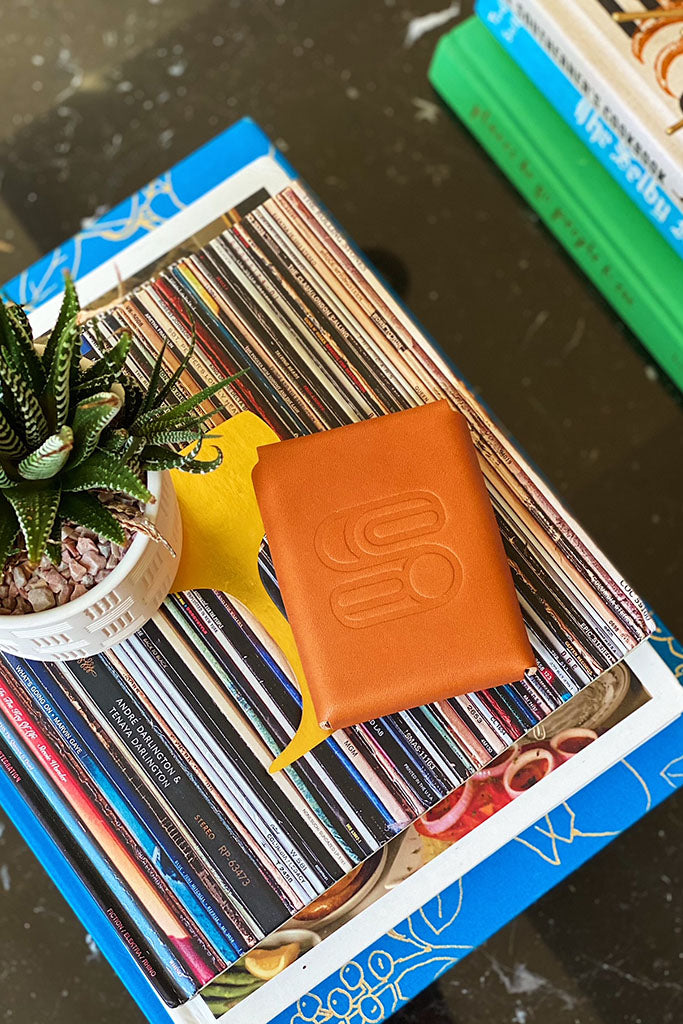 Leather playing card case with the Sound As Ever Logo stamped into the leather and sitting on top of books next to a spiky plant