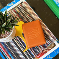 Leather playing card case with the Sound As Ever Logo stamped into the leather and sitting on top of books next to a spiky plant