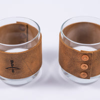 Handmade leather wrapped whiskey glasses with arrow design and brass buttons close up view