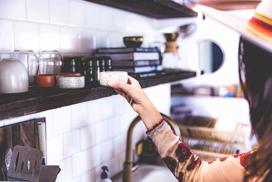 Woman in kitchen grabbing the white speckled clay mezcal copita from a shelf
