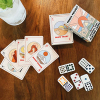 National park playing cards splayed on a table with their box, some dominos and a drink with a mint leaf