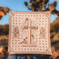 Two women holding the Sinner & Seeker organic cotton bandana in the desert. The design has two women next to a cross, joshua trees, UFOs, and snakes in an infinity shape