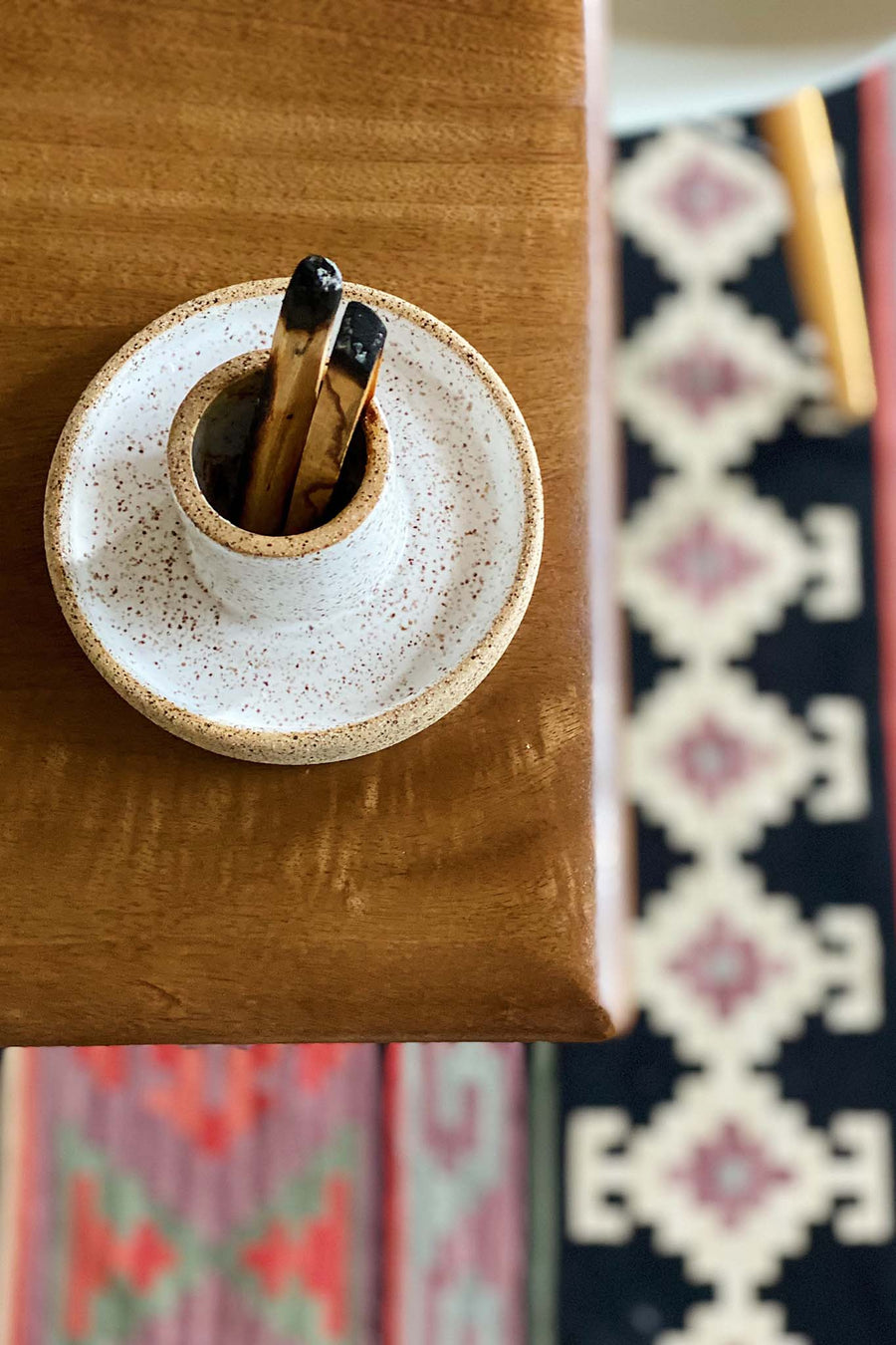 Palo santo holder and sage burning bowl made from white speckled clay with two burnt palo santo sticks  on a table with a patterned rug beneath