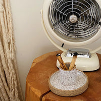 Palo santo holder and sage burning bowl made from white speckled clay with two burnt palo santo sticks next to a vintage fan on a wood side table