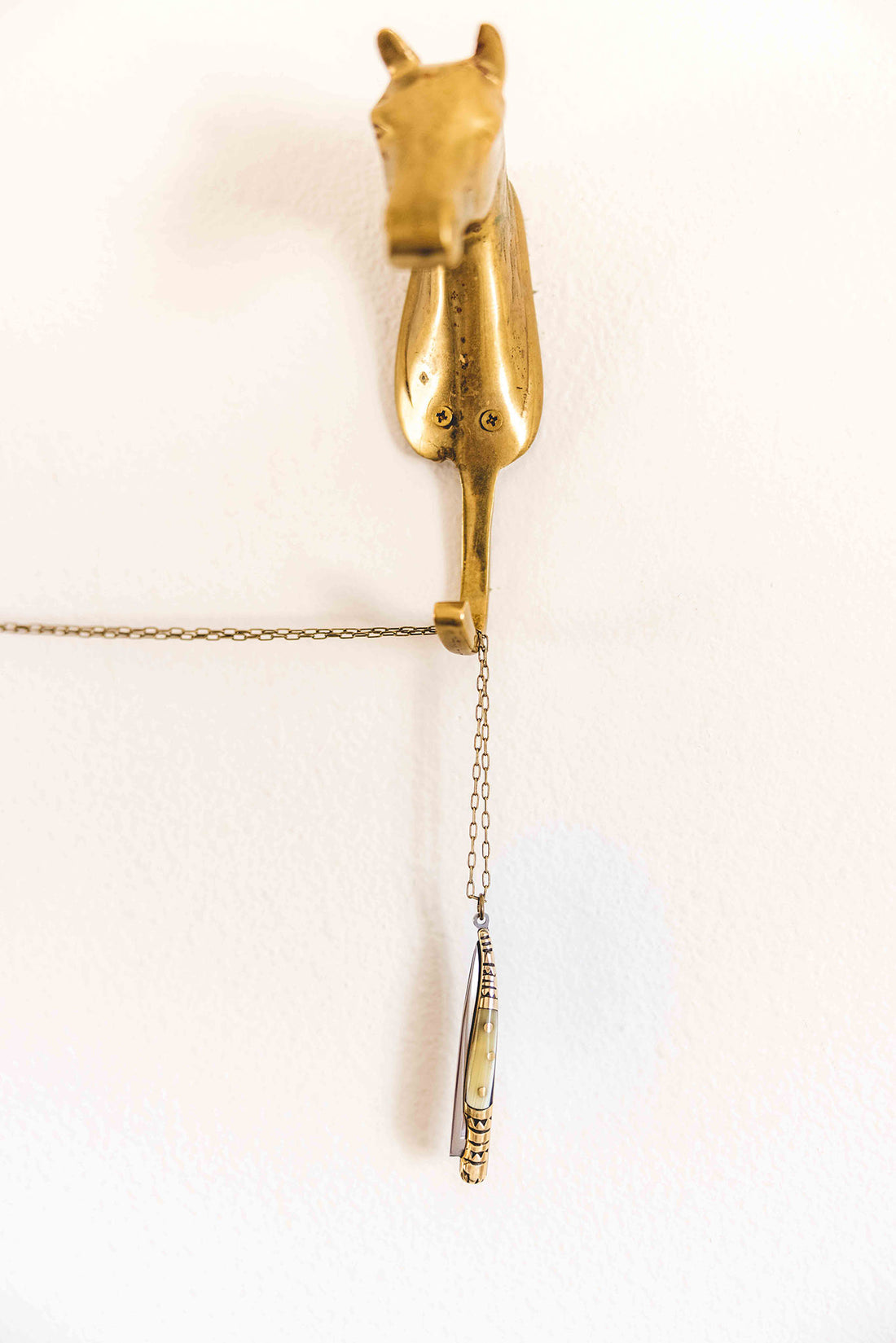 Pocket knife necklace made from brass and faux bull horn that hands with its brass chain from from a brass hook shaped like a horse head