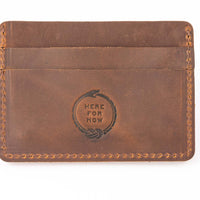 Slim minimalist wallet made from brown genuine leather with two card pockets shown and embossed with "Here for Now" Ouroboros design