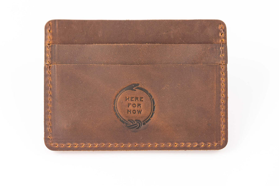 Slim minimalist wallet made from brown genuine leather with two card pockets shown and embossed with "Here for Now" Ouroboros design