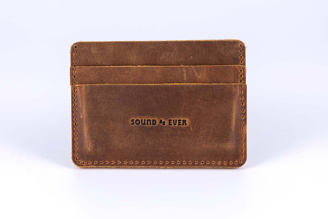 Close up view of slim minimalist wallet made from brown genuine leather with two card pockets shown and embossed with text "Sound As Ever"