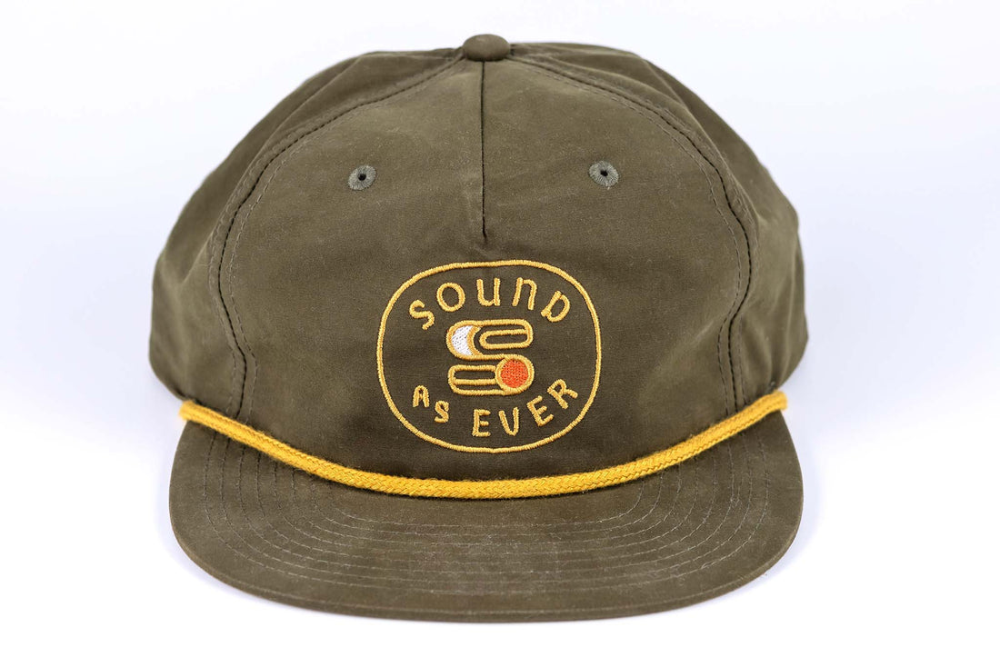 Close up view of Olive green colored Sound As Ever snapback cap featuring yellow embroidered logo