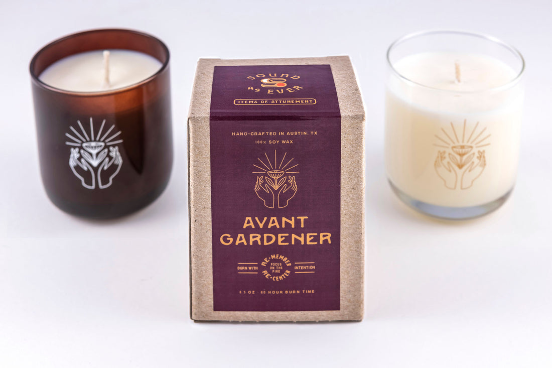 Soy wax candle in "Avant Gardener" scent with design of two hands open with a hovering flower above