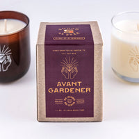 Soy wax candle in "Avant Gardener" scent with design of two hands open with a hovering flower above