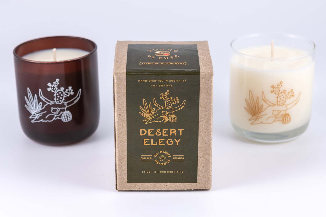 Soy wax candle in "Desert Elegy" scent with design showing a lounging woman figure or skull of a bovine with horns and cactus on top