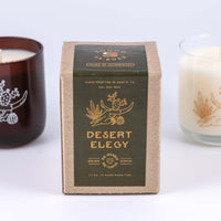 Soy wax candle in "Desert Elegy" scent with design showing a lounging woman figure or skull of a bovine with horns and cactus on top