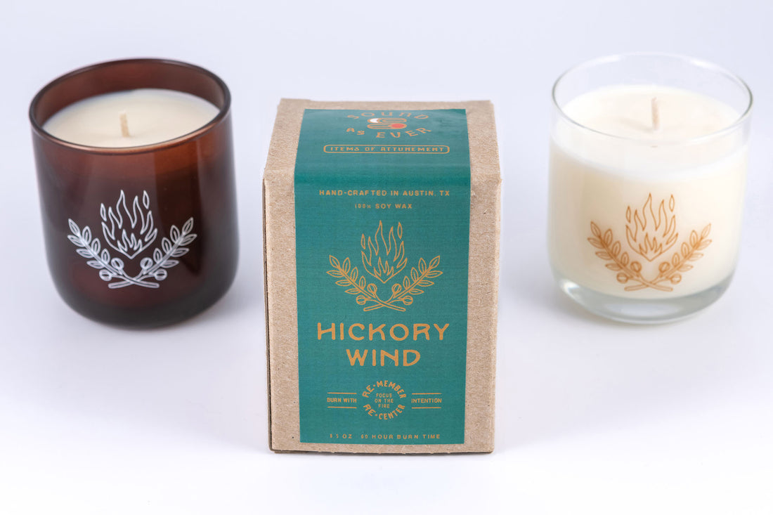 Soy wax candle in "Hickory Wind" scent showing design of two plant branches and fire above