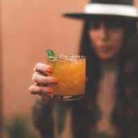 Soy wax candle clear glass shown after being cleaned and now filled with a mixed drink held up by a woman in background