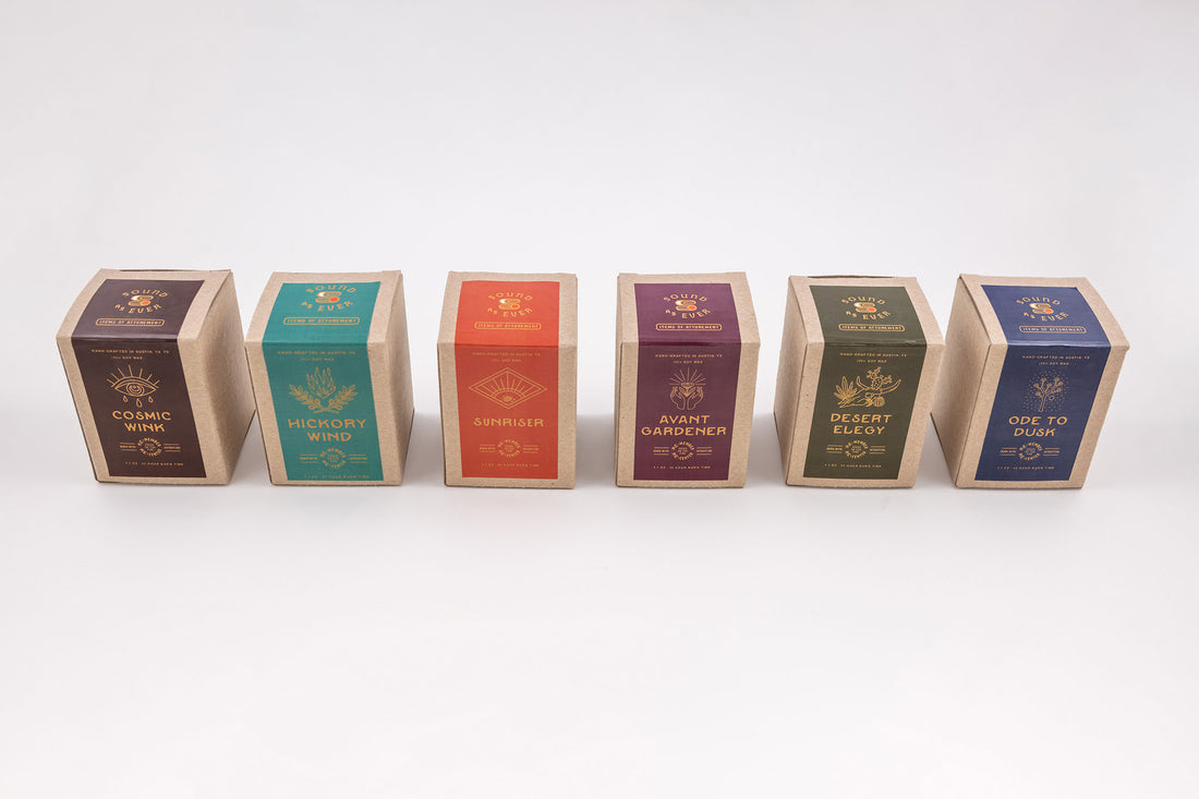 Soy wax candles in boxes showing six different options- cosmic wink, hickory wind, sunriser, avant gardener, desert elegy, and ode to dusk 