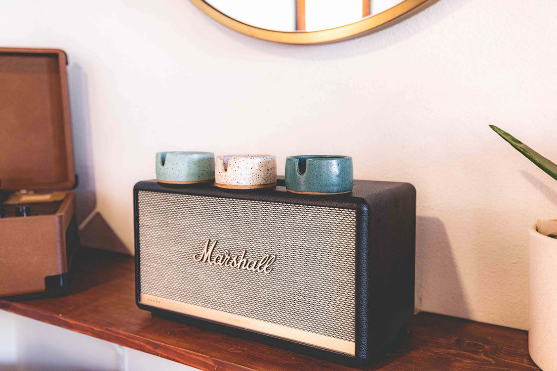 Three stoneware ashtrays each a different color of speckled clay- white, light blue, and darker greenish blue on top of a Marshall speaker