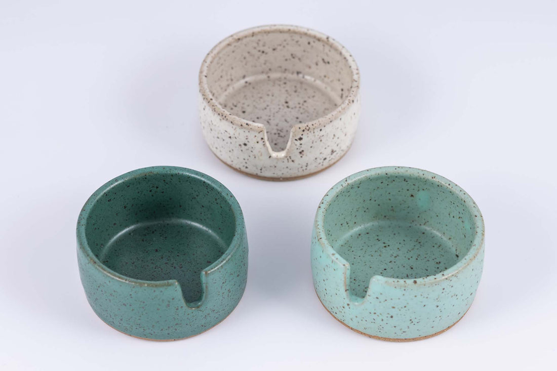 Closer view of three stoneware ashtrays each a different color of speckled clay- white, light blue, and darker greenish blue
